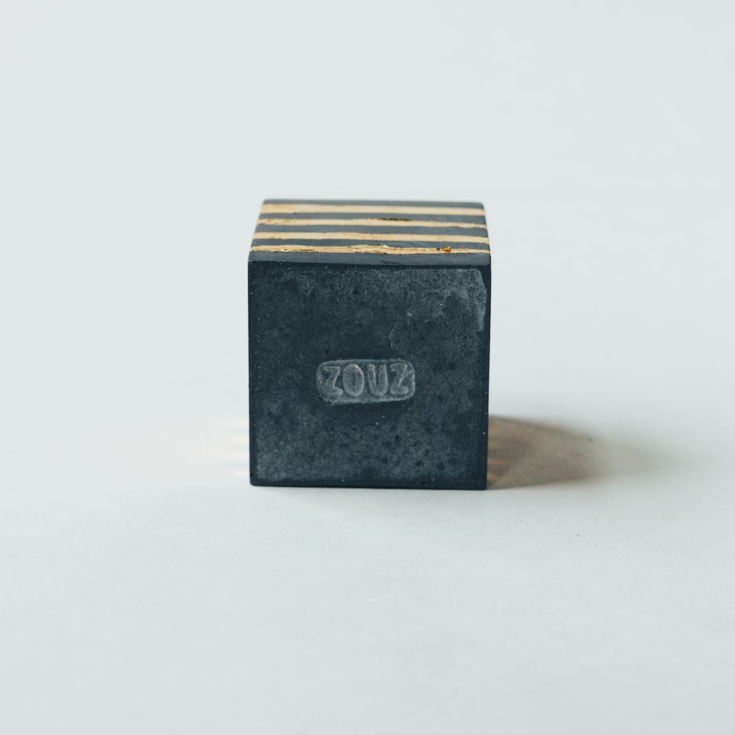ZOUZ natural incense cube shaped concrete incense cone burner with “ZOUZ” engraved on the bottom.