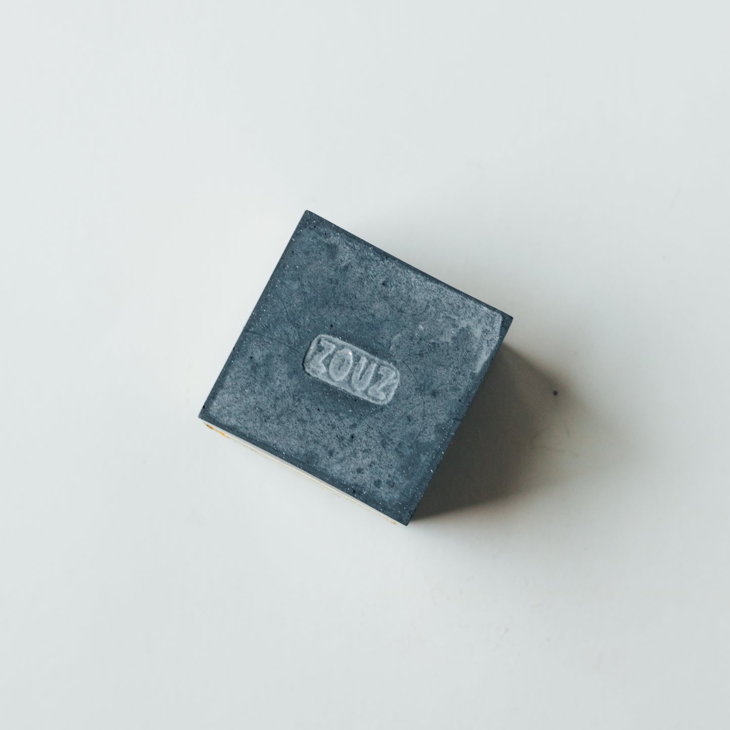 ZOUZ natural incense cube shaped concrete incense cone burner with “ZOUZ” engraved on the bottom.