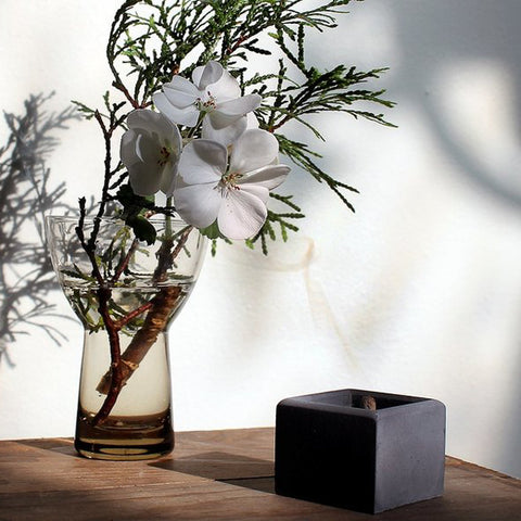 ZOUZ natural incense cone burning in a cube shaped incense burner on a table next to a vase with flowers