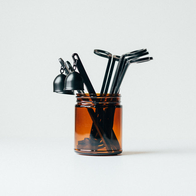 Amber jar filled with assorted candle accessories, including wick trimmers and candle snuffers.