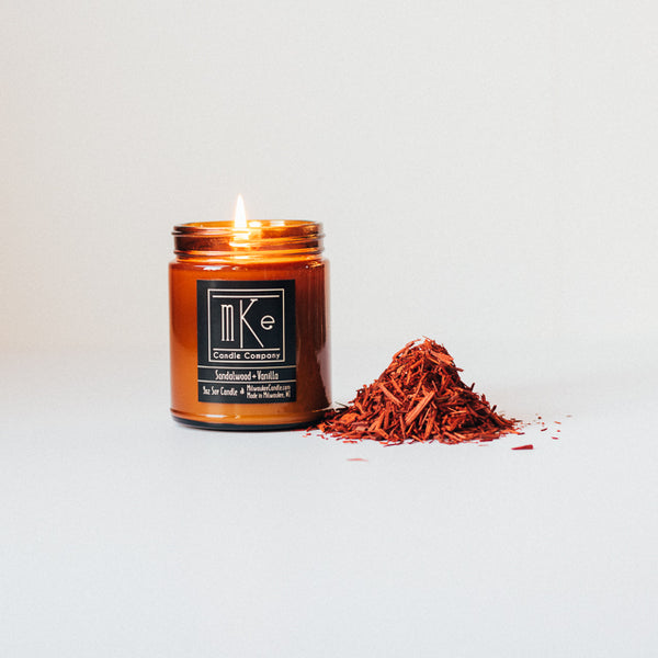 Lit 9 ounce Sandalwood and Vanilla soy candle with a small pile of sandalwood chips