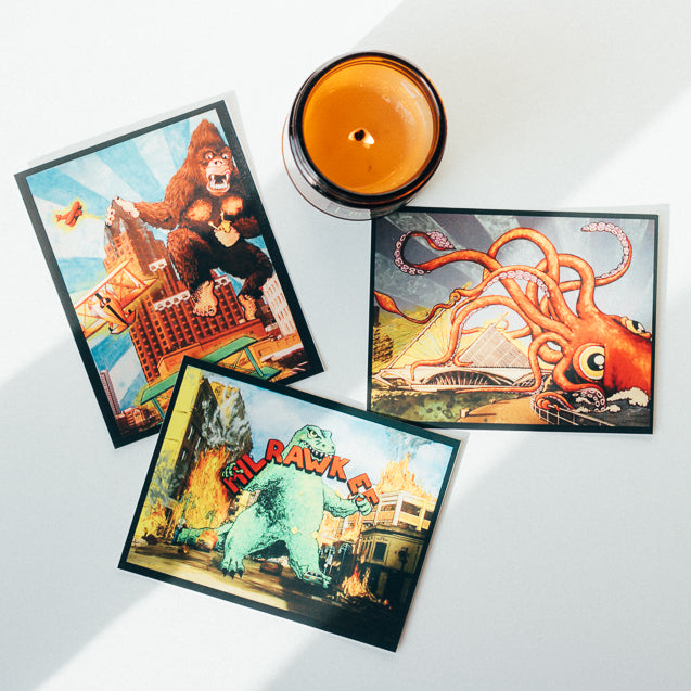 Top view of 9 ounce soy candle with 3 decorative art prints scattered around it