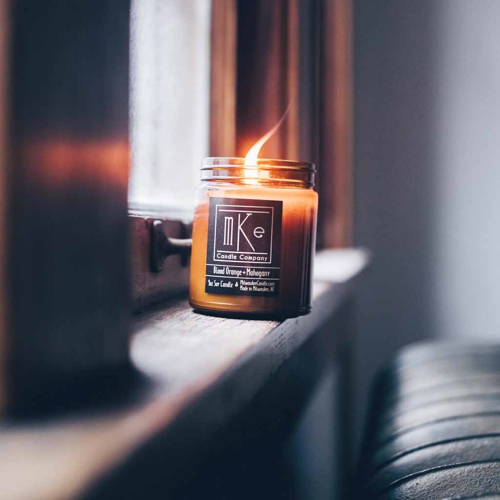 Lit 9 ounce amber jar soy candle sitting on a windowsill