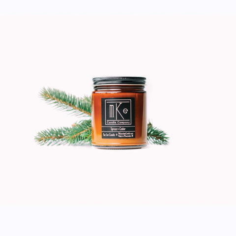 9 ounce Spruce and Cedar amber jar soy candle with evergreen branches in the background