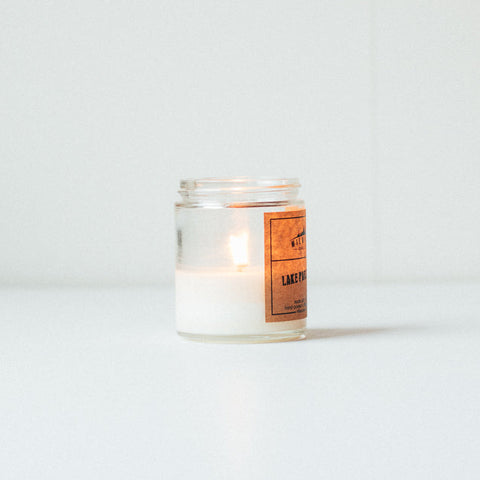 Lit 6 ounce clear jar soy wax candle with kraft paper label.