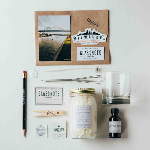 DIY candle making kit contents: kraft paper placemat, Milwaukee Candle Co sticker, Glassnote Candle Bar sticker, Milwaukee photocard, pencil, wick, wick stickum, whisk, glass, soy wax jar, fragrance oil vial, label, clothespin, caution sticker, match box