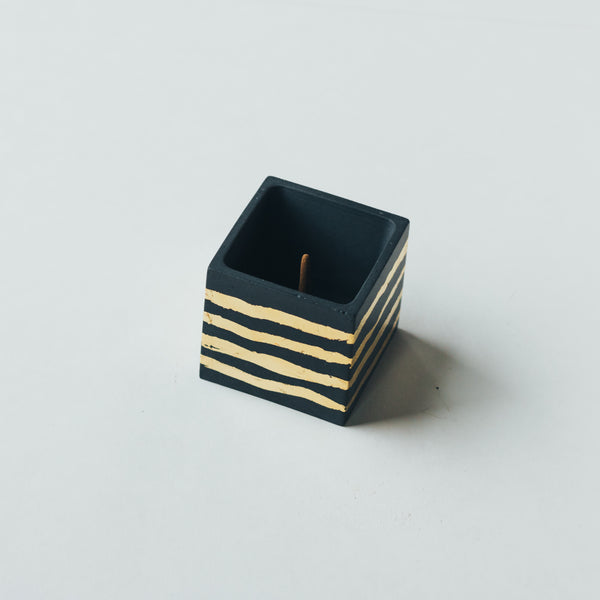 ZOUZ natural incense cube shaped concrete incense cone burner. Dark gray with gold foil strips on the sides.