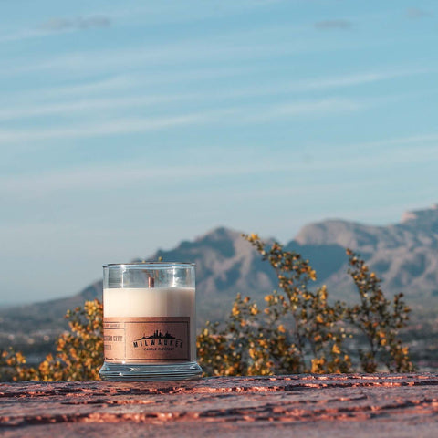 12 ounce ButterCream City Vanilla soy wax candle on a rocky surface with a mountainscape in the background.