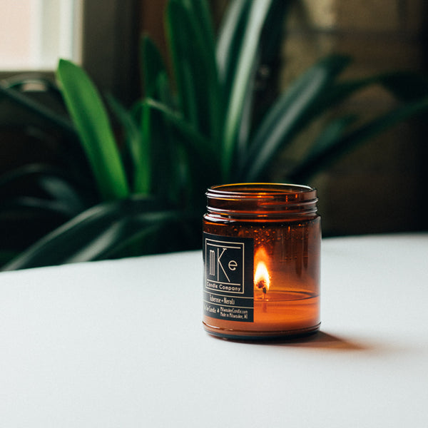 Lit 9 ounce amber jar soy candle with plant in background